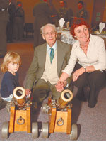 Three people kneel down in front of two cannons. 