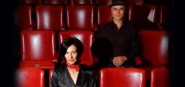 Two people dressed in black sitting in red seats. 