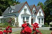 A white house with red trim and roses in the foreground. 