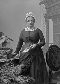 Black and white photo of Mary Bisley standing in a dress. 