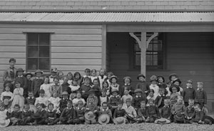 Black and white photo of Jane Bond and children outside a school house. 