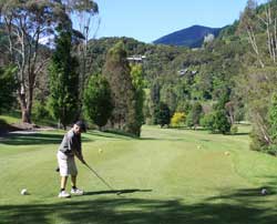 A man tees off at the top of a fairway overlooking trees and hills. 